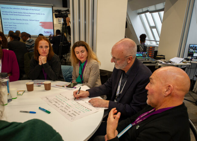 A table of practitioners in discussion, as one writes down collective notes.