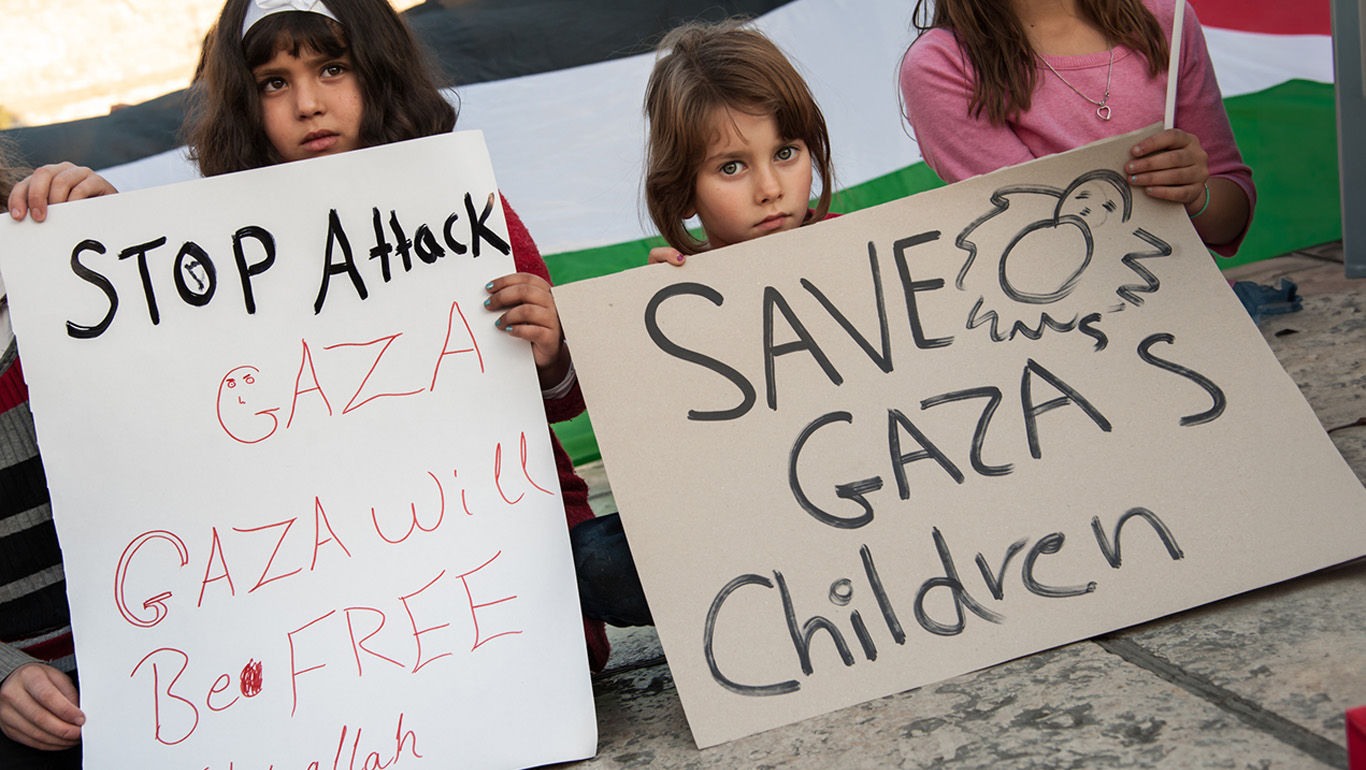 Palestinian children hold signs protesting Israeli military strikes on Gaza